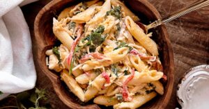 A mouth-watering creamy pasta salad with fresh vegetables served in a rustic wooden bowl.
